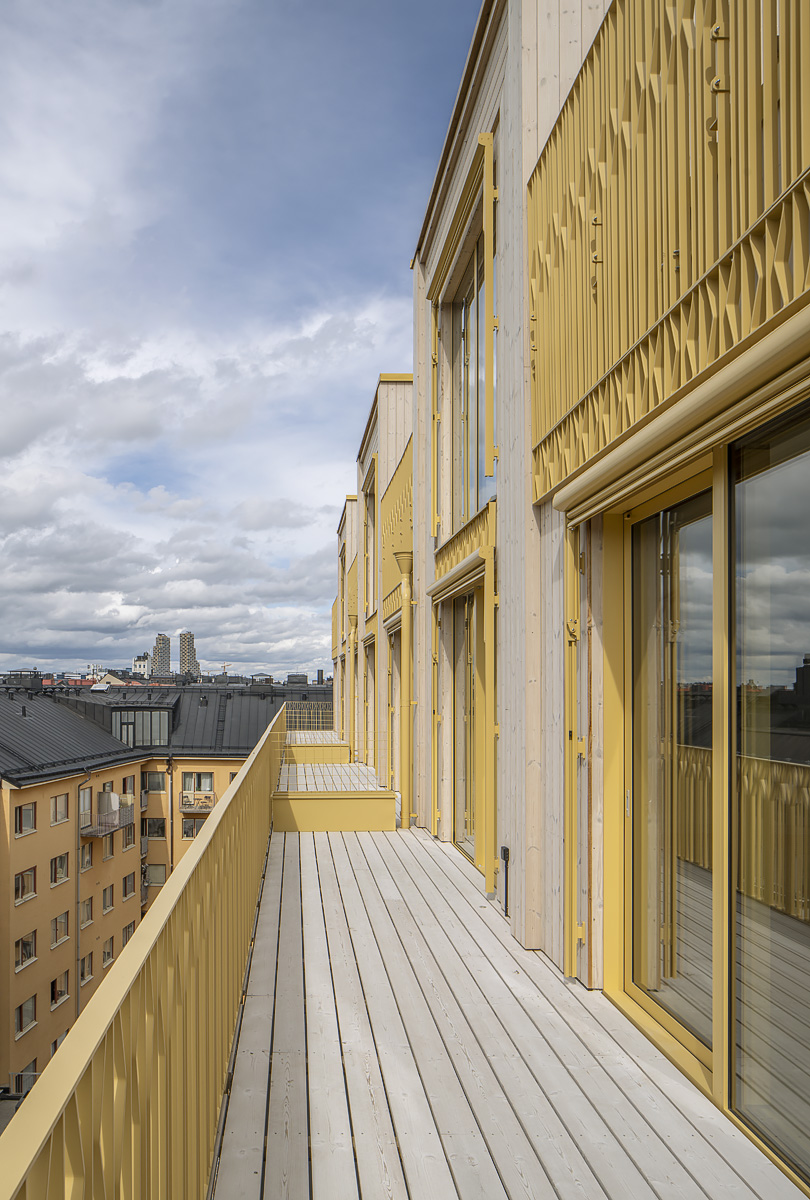 Gårdslundens gula träfasad med balkonger, sedd längs husets utsida.